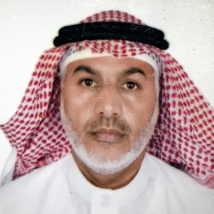 Portrait of a man in a white kandura and red-and-white ghutra with a black agal, looking at the camera.